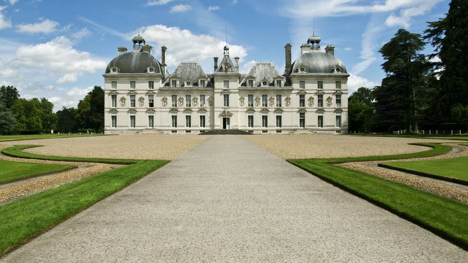 A large, symmetrical building with domed roofs and a central entrance, surrounded by well-manicured lawns and gravel paths.
