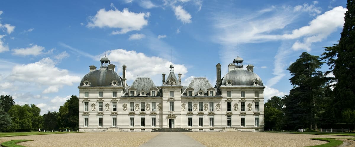 A large, symmetrical building with domed roofs and a central entrance, surrounded by well-manicured lawns and gravel paths.