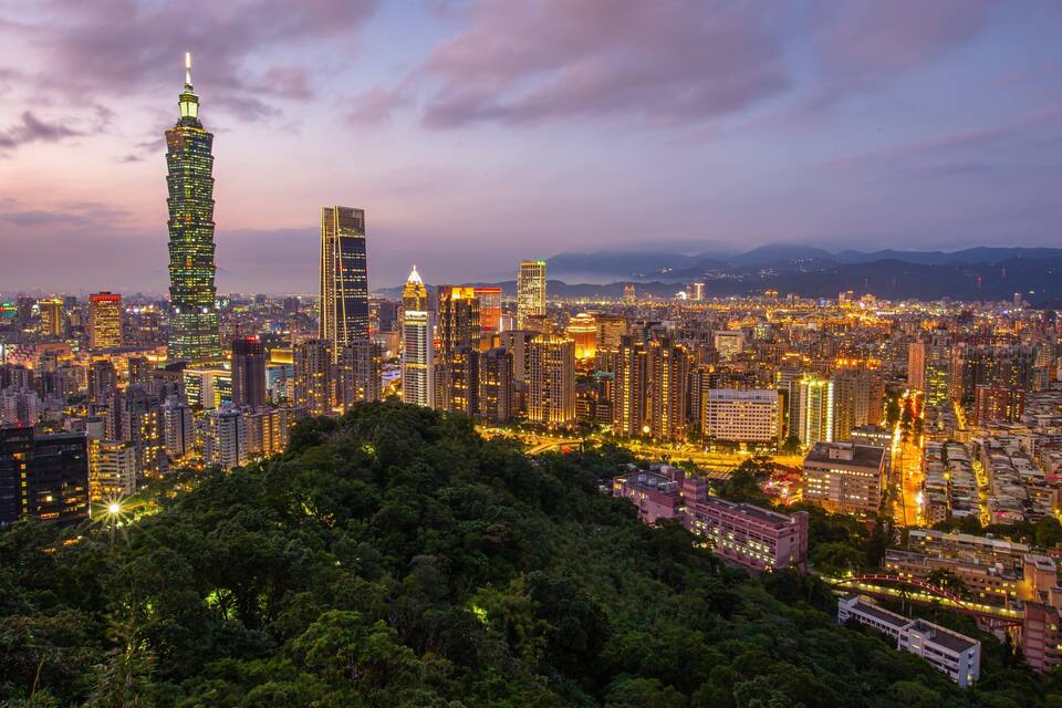 A cityscape at dusk with illuminated skyscrapers and a prominent tower.
