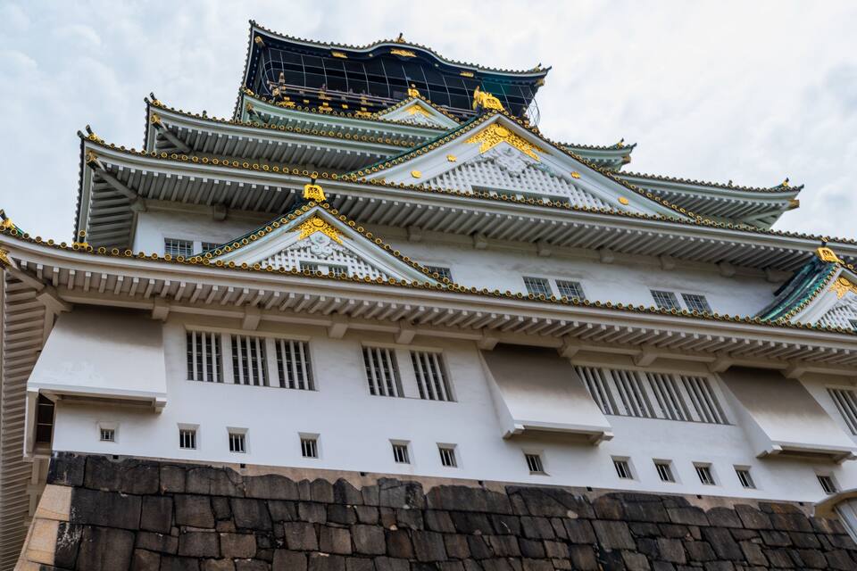 Een traditioneel Japans kasteel met meerdere verdiepingen, gedetailleerde gouden versieringen en een stenen fundament.
