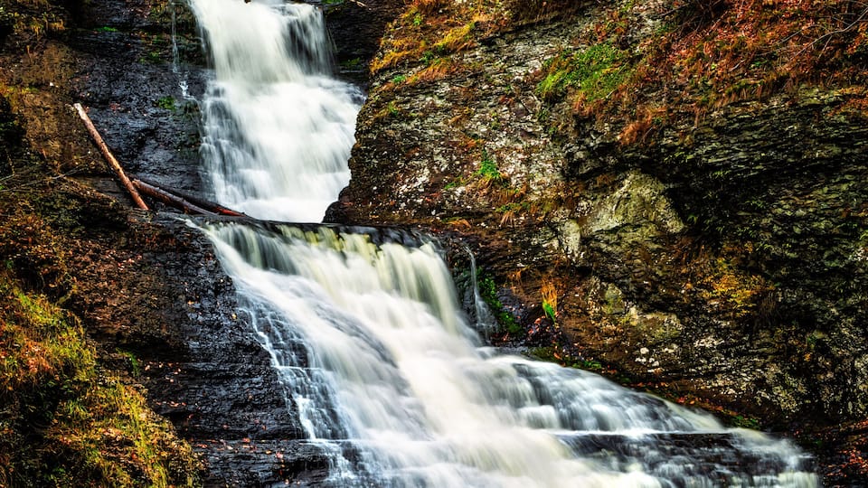 A multi-tiered waterfall surrounded by autumn foliage and a wooden viewing platform.