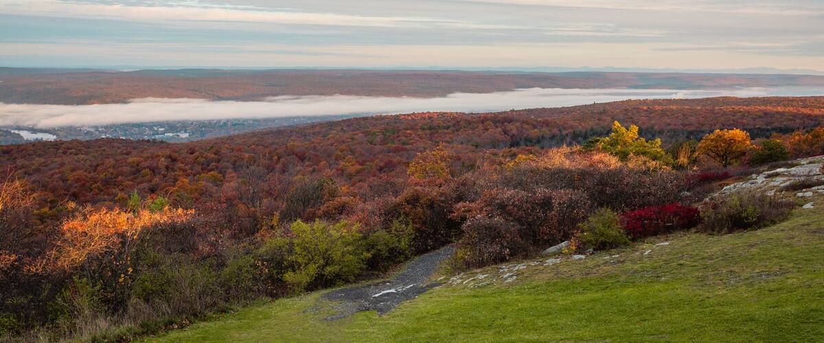 A mountainous landscape with autumn foliage, a valley below, and a distant mist-covered town.