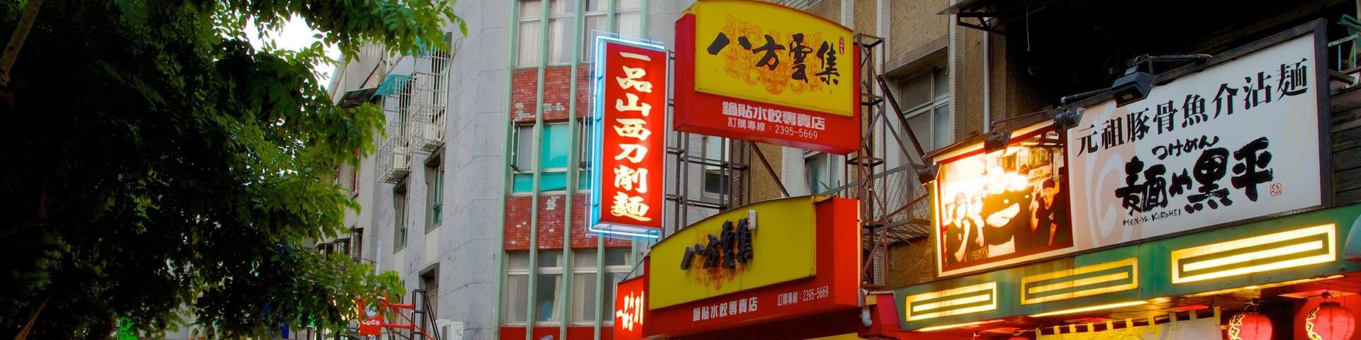 A busy street with various shops and signs, including a CoCo store and a restaurant with bright signage.