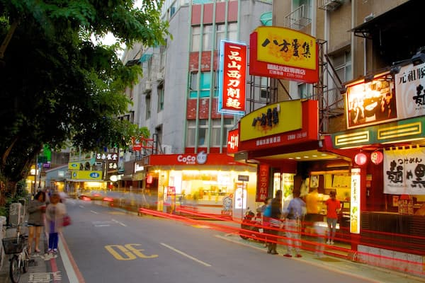 A busy street with various shops and signs, including a CoCo store and a restaurant with bright signage.
