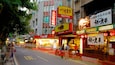 A busy street with various shops and signs, including a CoCo store and a restaurant with bright signage.