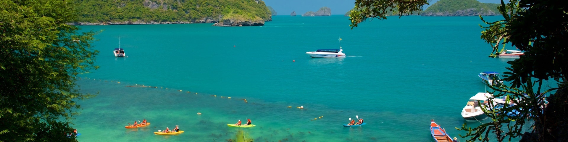 A turquoise sea with boats, kayaks, and a beach.