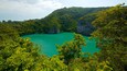 Un lac turquoise, bordé d’une forêt verdoyante et de falaises rocheuses.