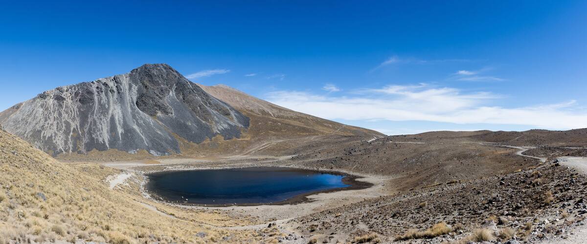 A mountainous landscape with a clear blue sky, a rocky terrain, and a small lake.