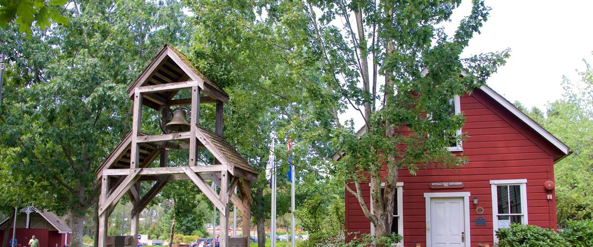 A wooden bell tower, a red building, and a bench in a park.