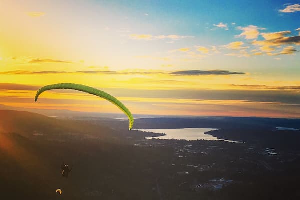 En paraglider flyver over en dal med solnedgang i baggrunden.