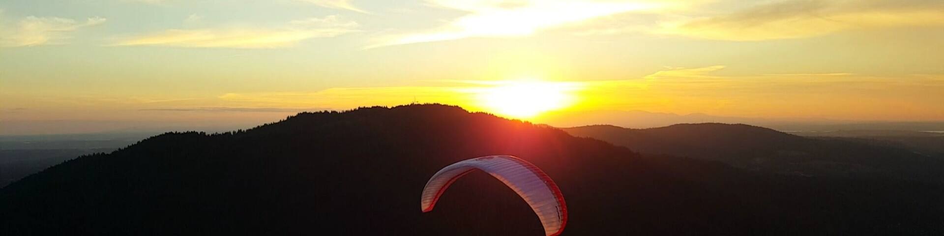 A person paragliding over a hilly landscape at sunset.
