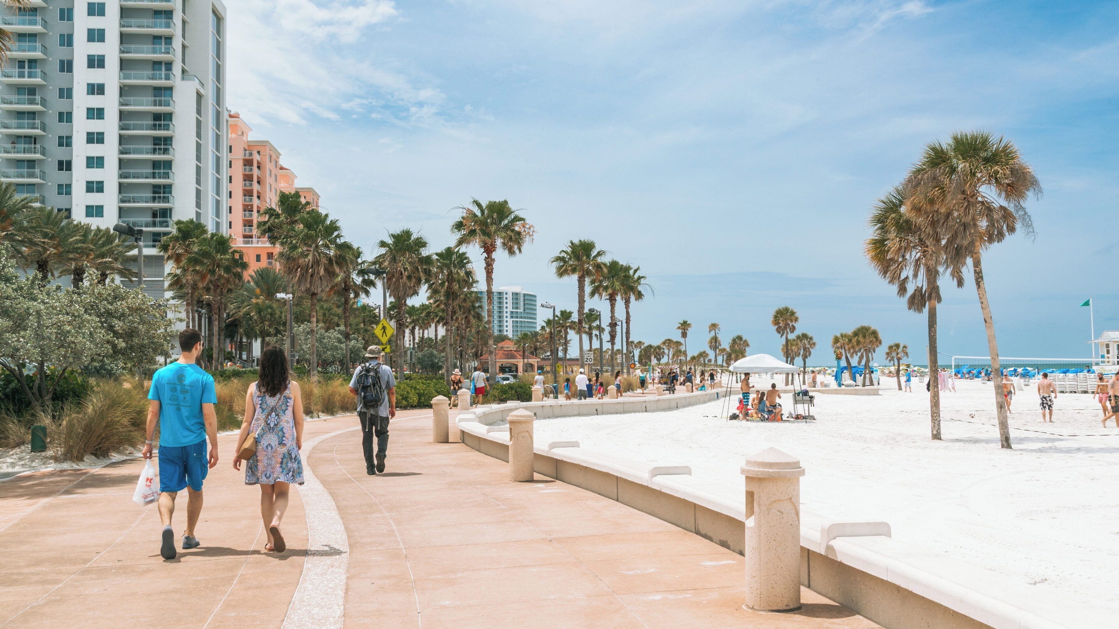 Couples stroll along Clearwater Beach boardwalk under sunny skies in Florida, enjoying the vibrant atmosphere and coastal views