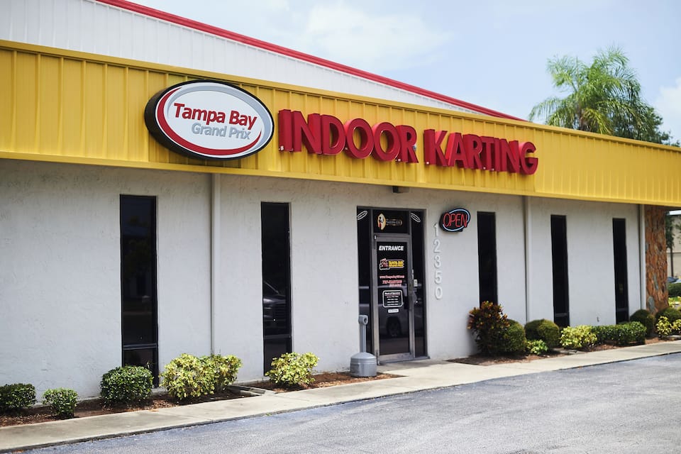 Edifício do Tampa Bay Grand Indoor Karting, com fachada amarela e uma placa indicando a entrada.