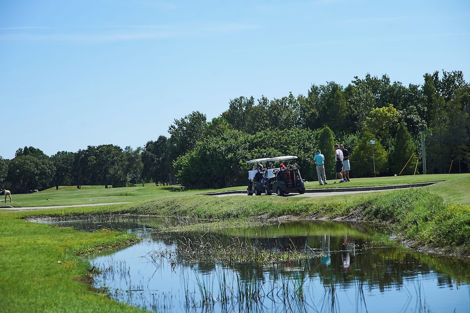 A golf course with a pond, a golf cart, and people playing golf.