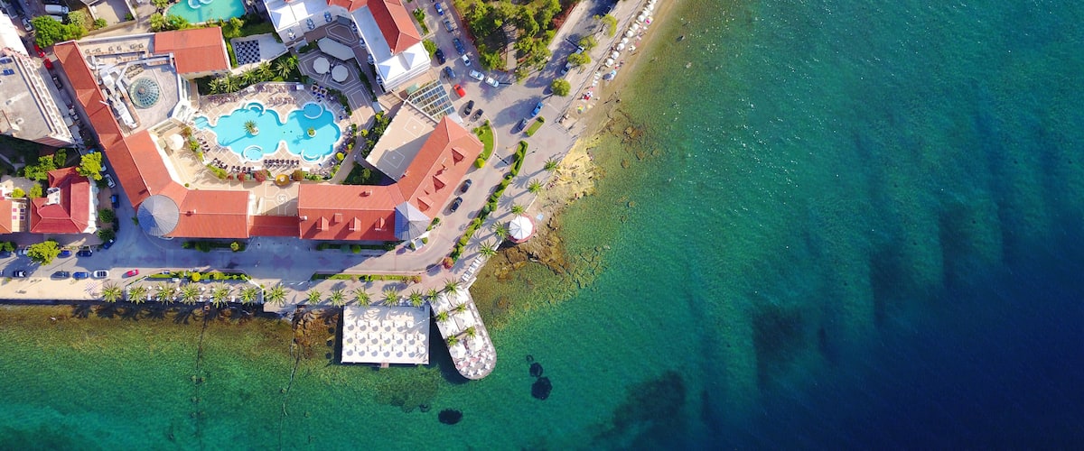 An aerial view of a coastal resort with a swimming pool, beach, and hotel buildings.