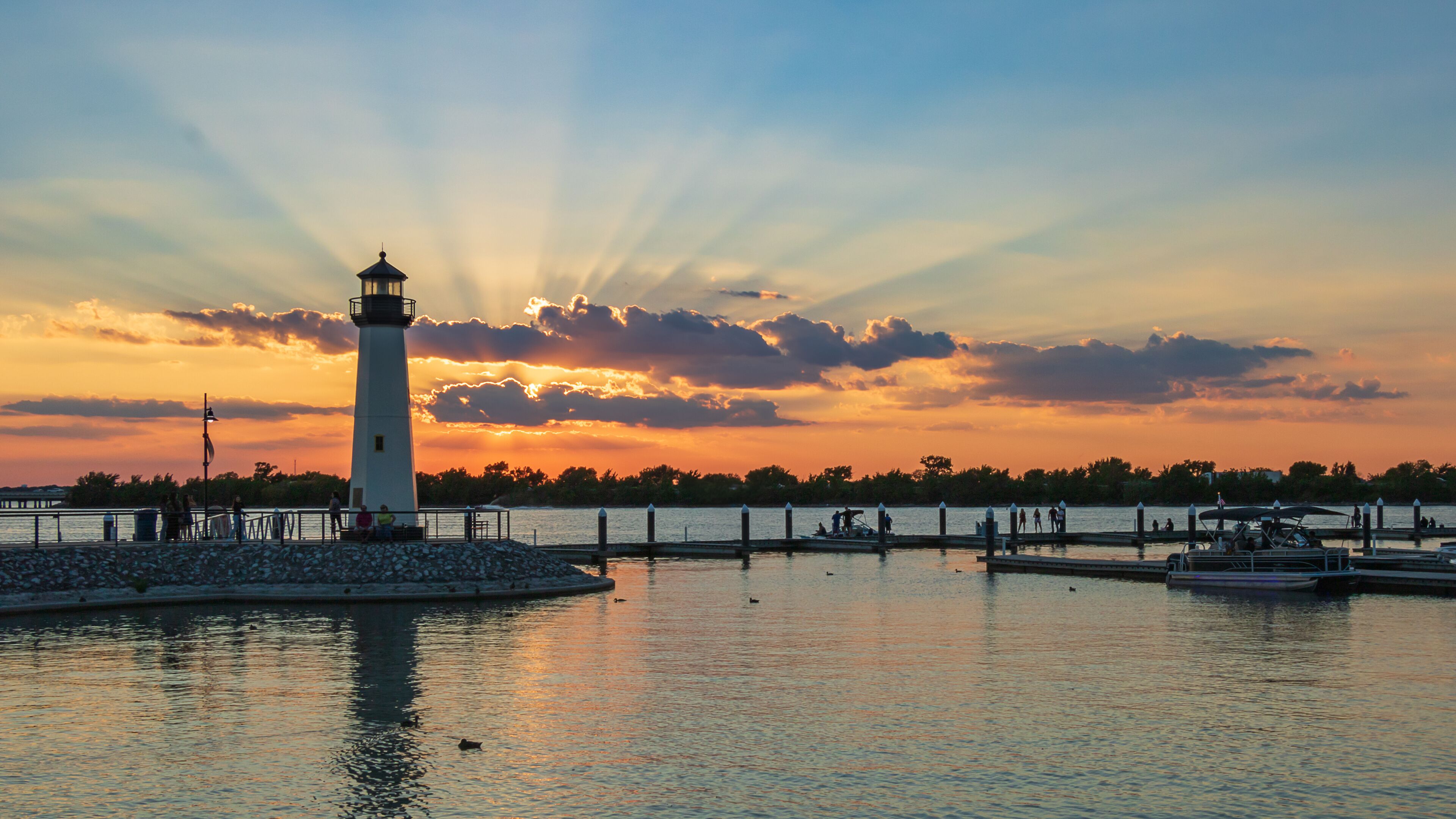 A lighthouse by a calm waterfront at sunset.