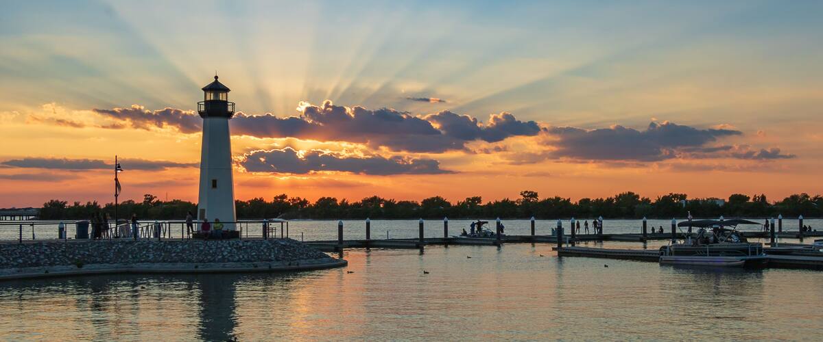 A lighthouse by a calm waterfront at sunset.