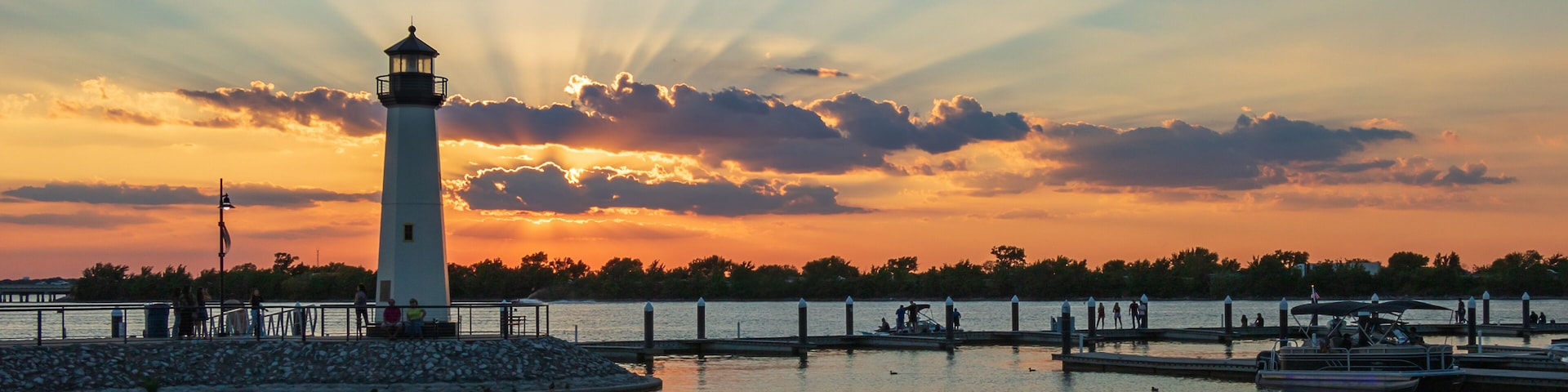 A lighthouse by a calm waterfront at sunset.