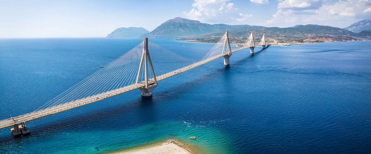 A suspension bridge over a deep blue sea with clear skies and distant mountains.