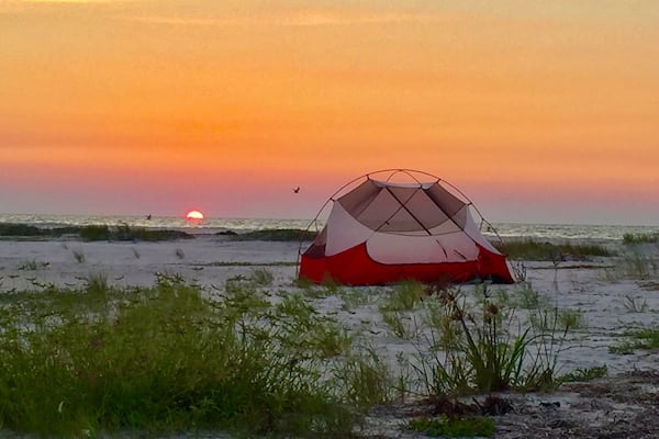 Une tente rouge et blanche sur une plage, au coucher du soleil.