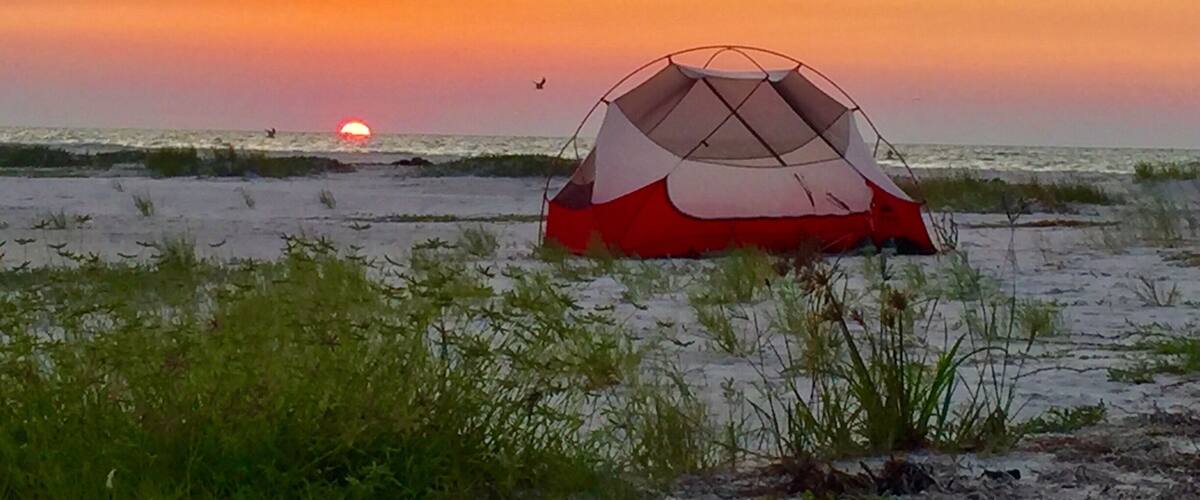 A red and white tent on a beach at sunset.