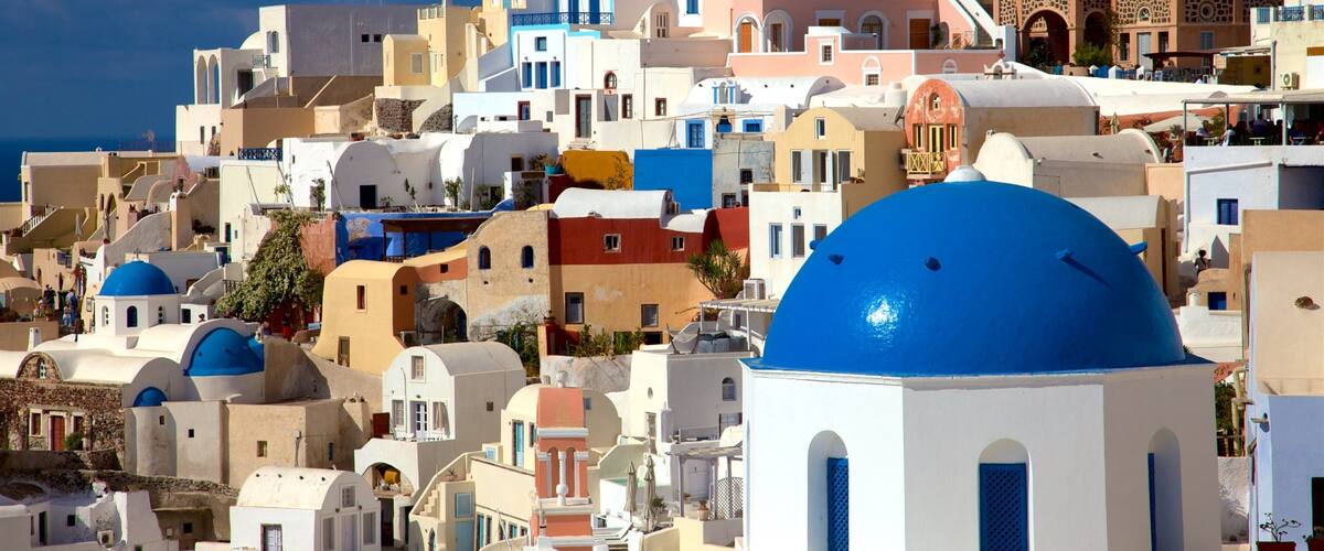 A coastal town with white and pastel-colored buildings, blue domes, and a clear blue sky.
