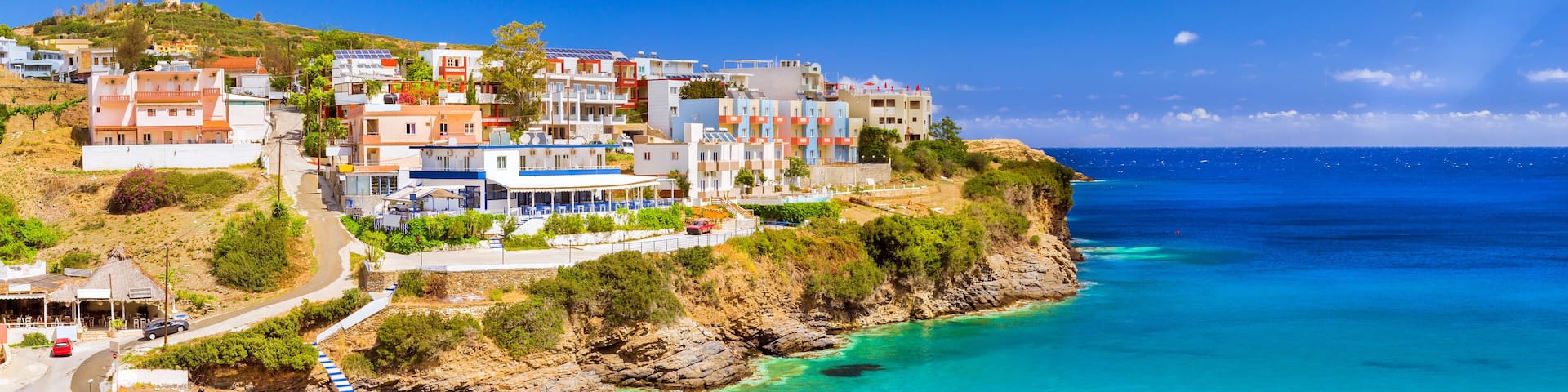 Sandy Varkotopos beach in sea bay of resort village Bali. Views of shore, washed by waves with sun loungers and parasols where sunbathing tourists. Greek houses stand on the rocky shore. Crete, Greece