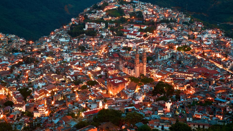 A densely populated hillside town at dusk with numerous buildings and a prominent church tower.