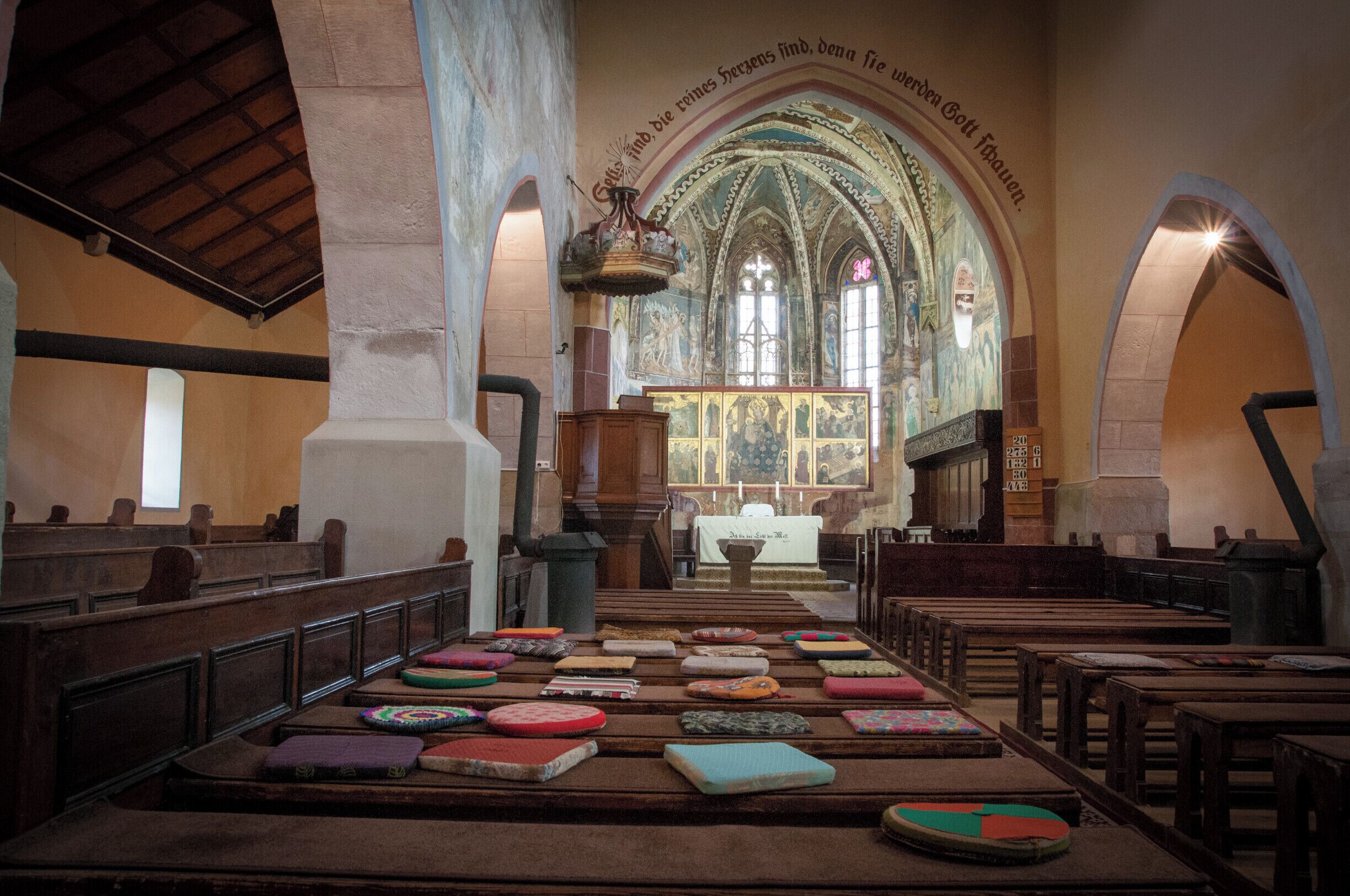 An interior of a church with pews, a pulpit, and a large stained glass window.