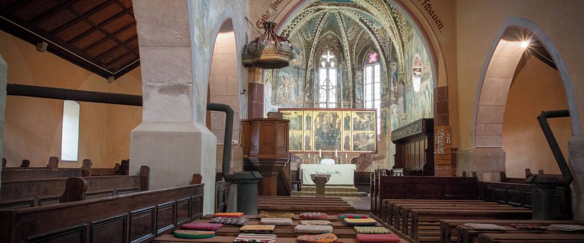 An interior of a church with pews, a pulpit, and a large stained glass window.