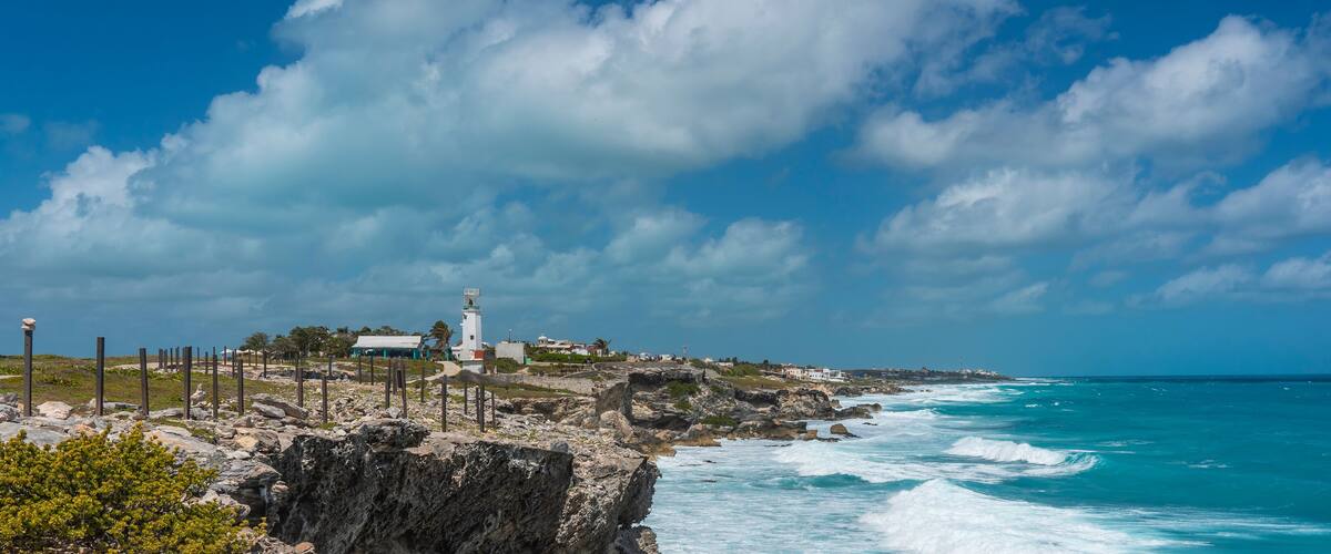 A coastal landscape with a lighthouse, rocky cliffs, and turquoise ocean waves.