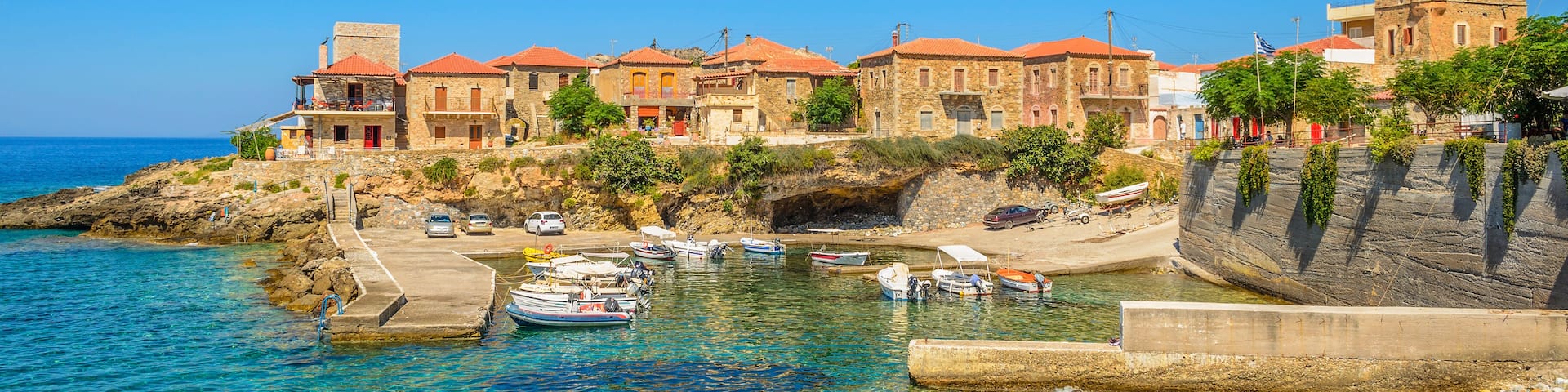 A coastal town with clear waters, boats docked at a pier, and buildings with red roofs.