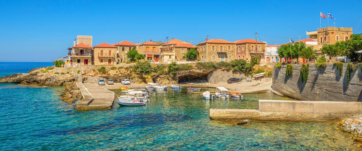 A coastal town with clear waters, boats docked at a pier, and buildings with red roofs.
