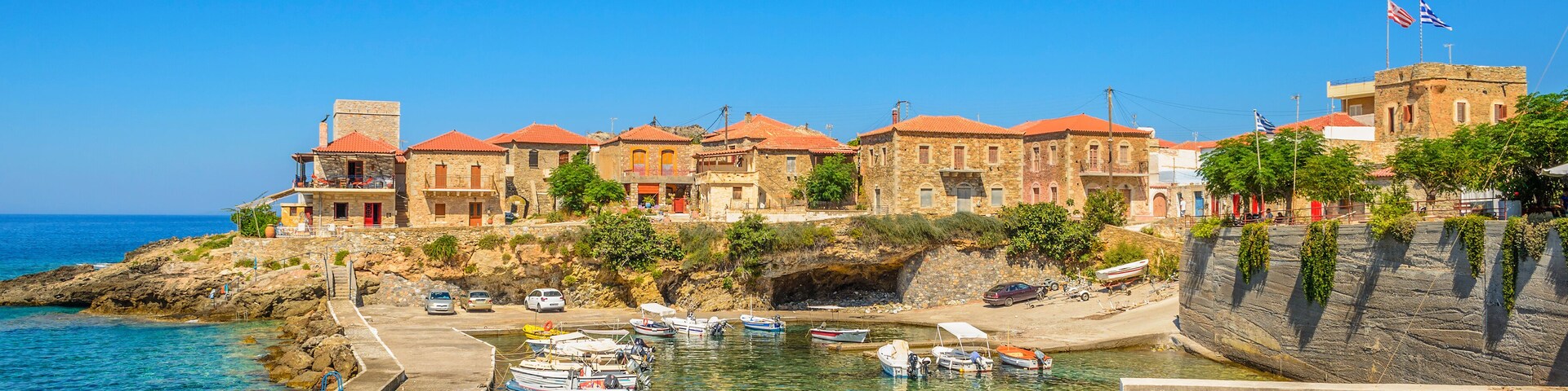 A coastal town with clear waters, boats docked at a pier, and buildings with red roofs.