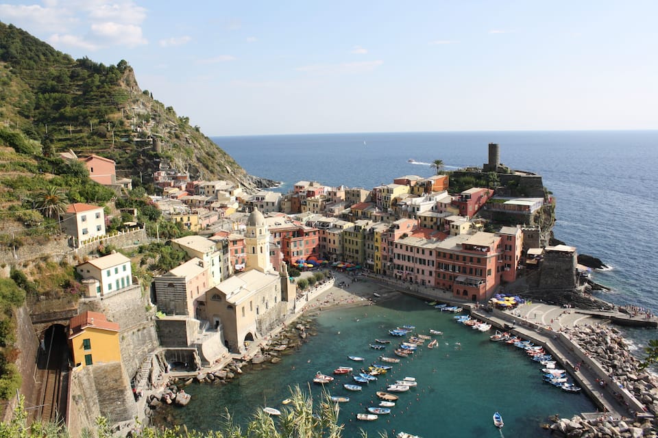 A coastal town with colorful buildings, a harbor with boats, and a cliff overlooking the sea.