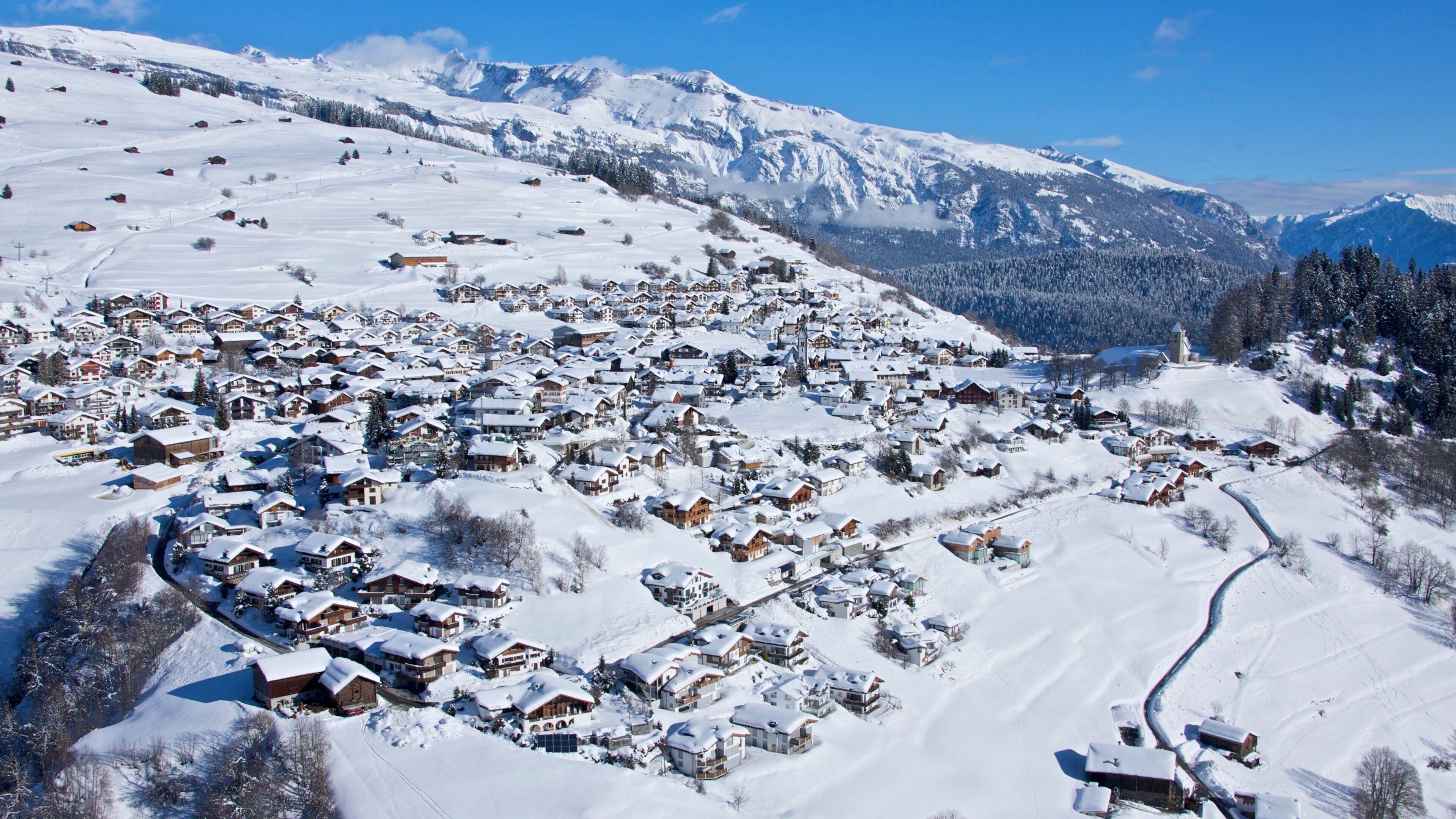 A snow-covered village with houses and mountains in the background.
