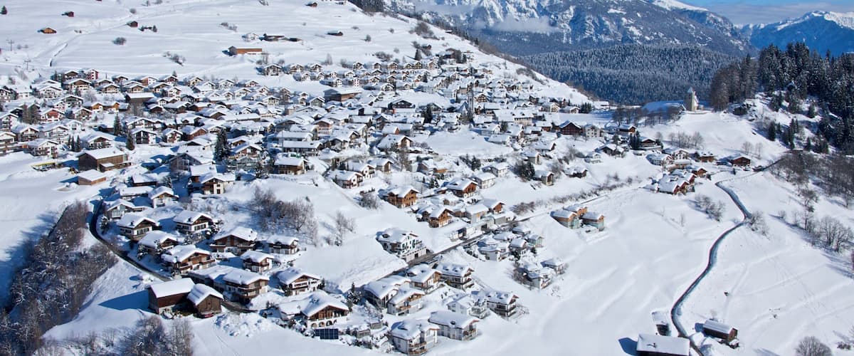 A snow-covered village with houses and mountains in the background.