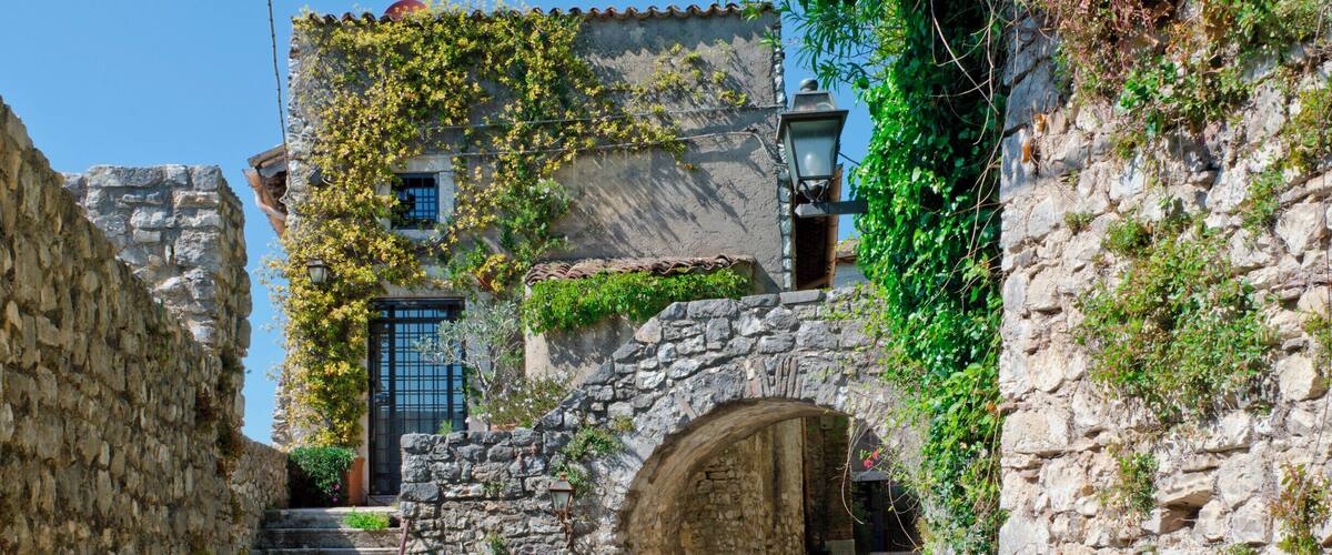 A stone staircase leading up to a building with a wooden door, surrounded by greenery and stone walls.