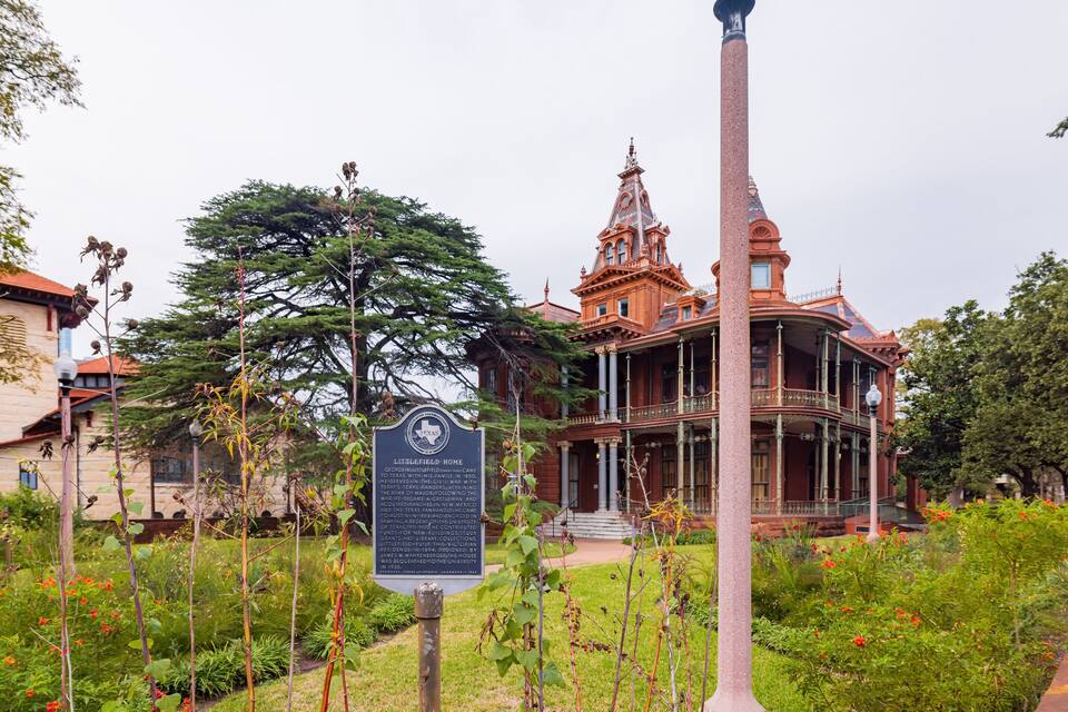 A historic building with a tower, surrounded by a garden with various plants and flowers.