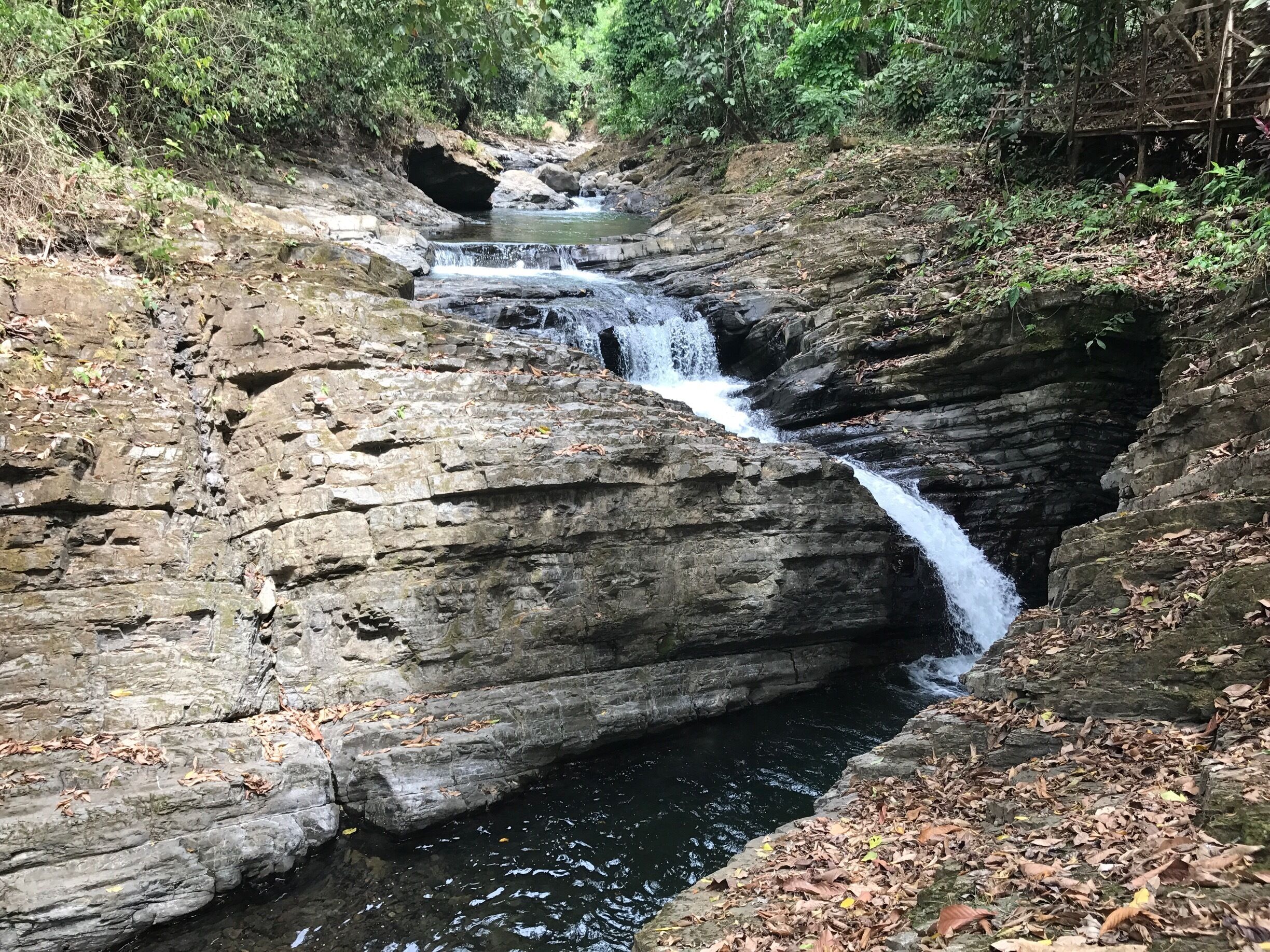 A multi-tiered waterfall cascading over rocky terrain surrounded by dense foliage.
