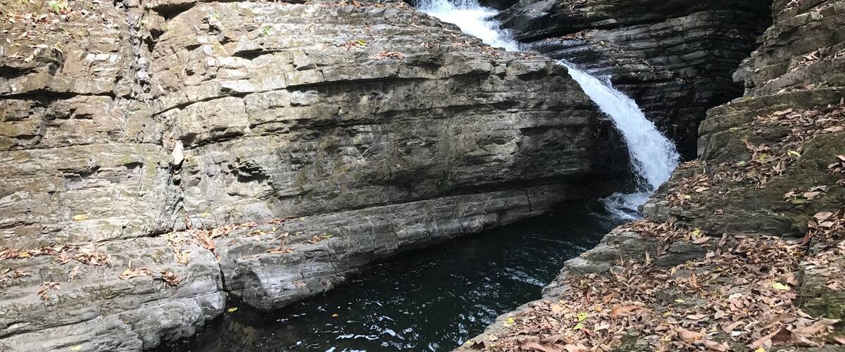 A multi-tiered waterfall cascading over rocky terrain surrounded by dense foliage.