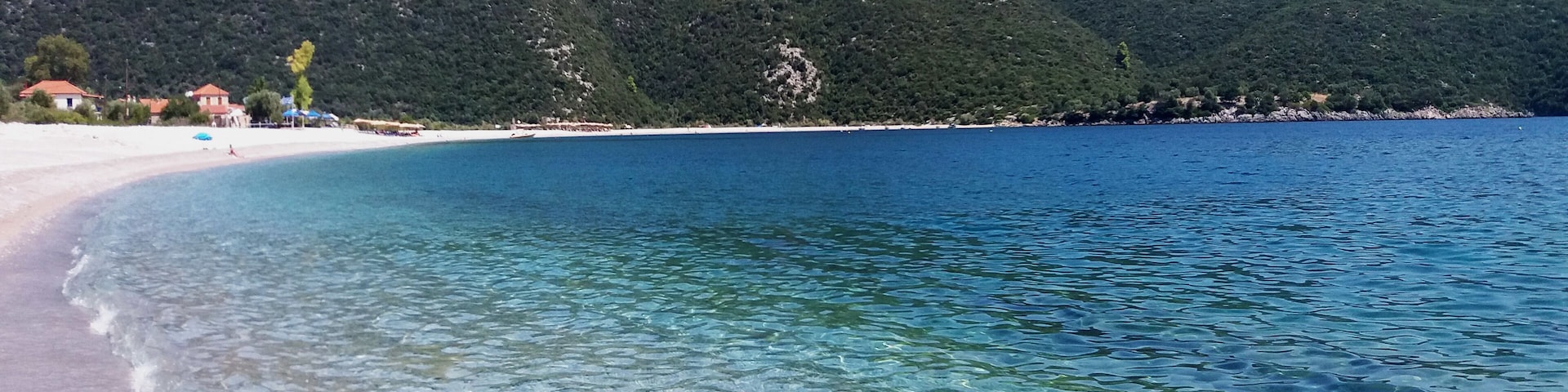 A clear beach with turquoise water, white sand, and green hills in the background.