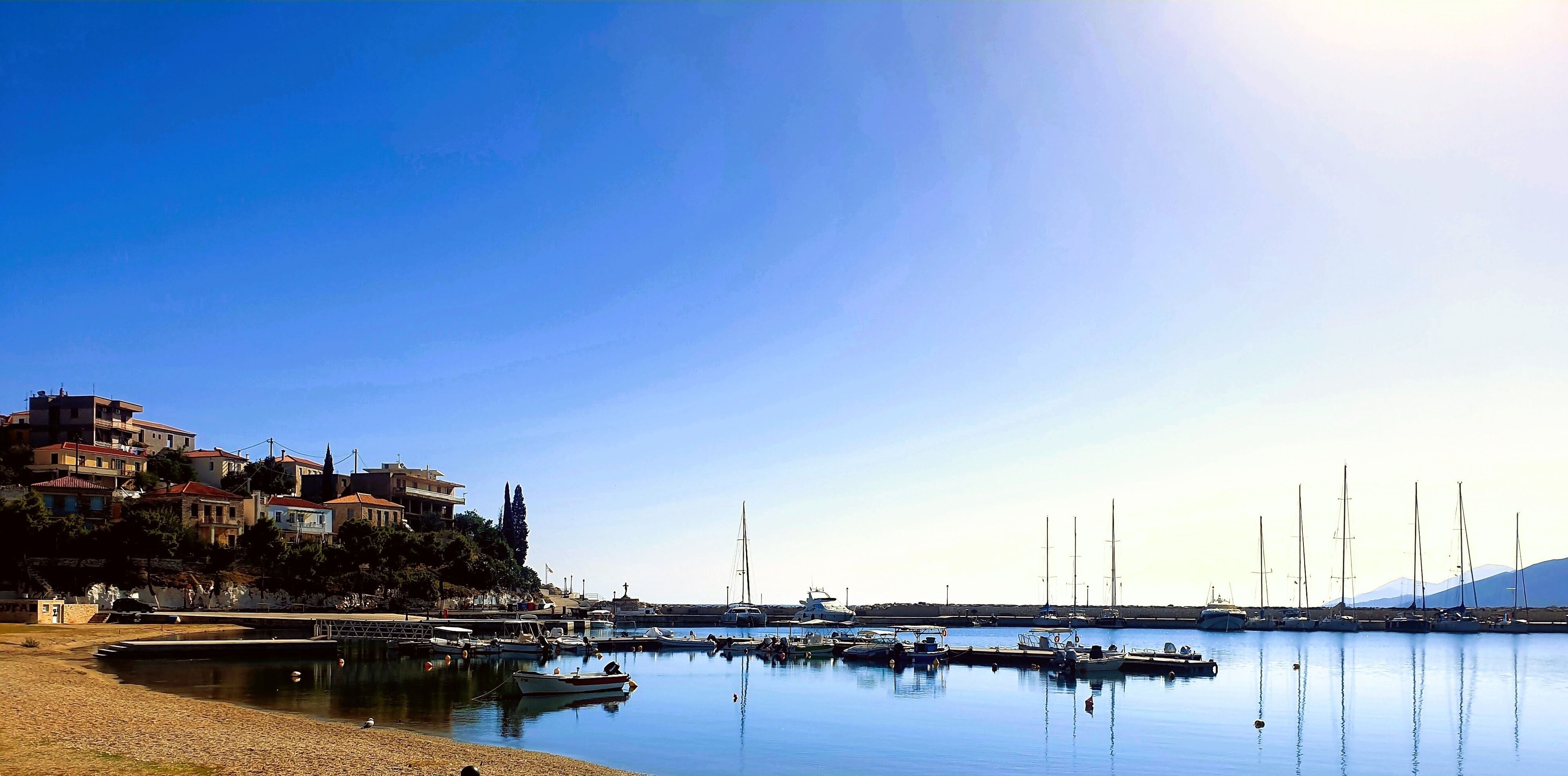 Astros a picturesque coastal town in Peloponnese, Greece, featuring its serene fishing shelter and clear azure waters. Small boats are visible floating peacefully near the shore.
