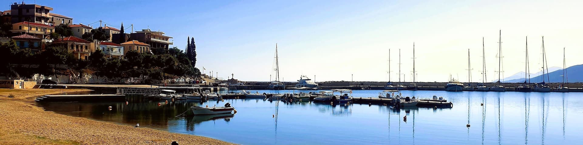 Astros a picturesque coastal town in Peloponnese, Greece, featuring its serene fishing shelter and clear azure waters. Small boats are visible floating peacefully near the shore.
