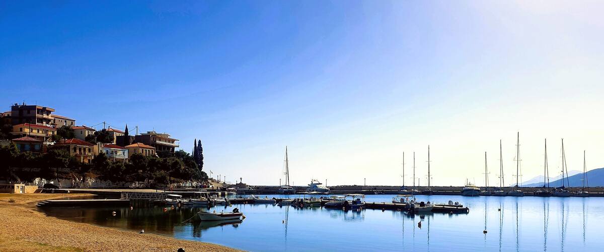 A calm harbor with boats, a sandy beach, and buildings on a hillside.