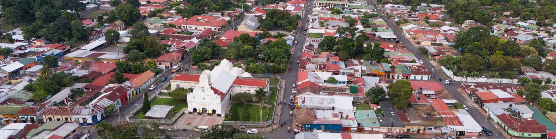 Aerial view of the San Marcos church surrounded by dense urban rooftops, lush green trees, and streets in San Marcos, Carazo, Nicaragua.