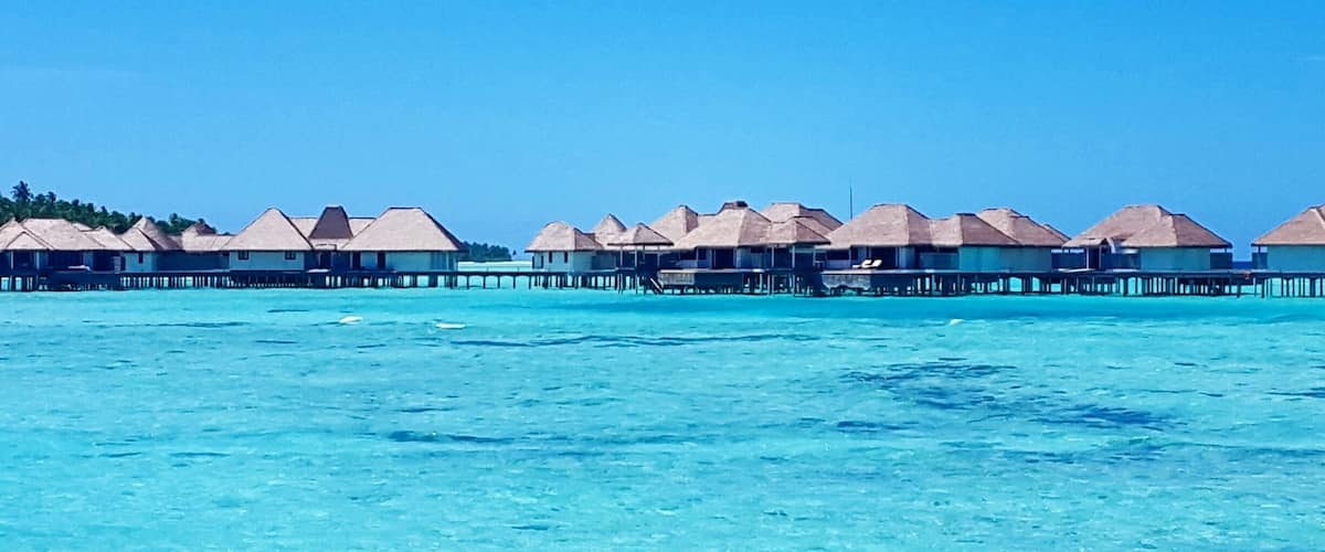 Overwater bungalows with thatched roofs on stilts in clear turquoise waters.