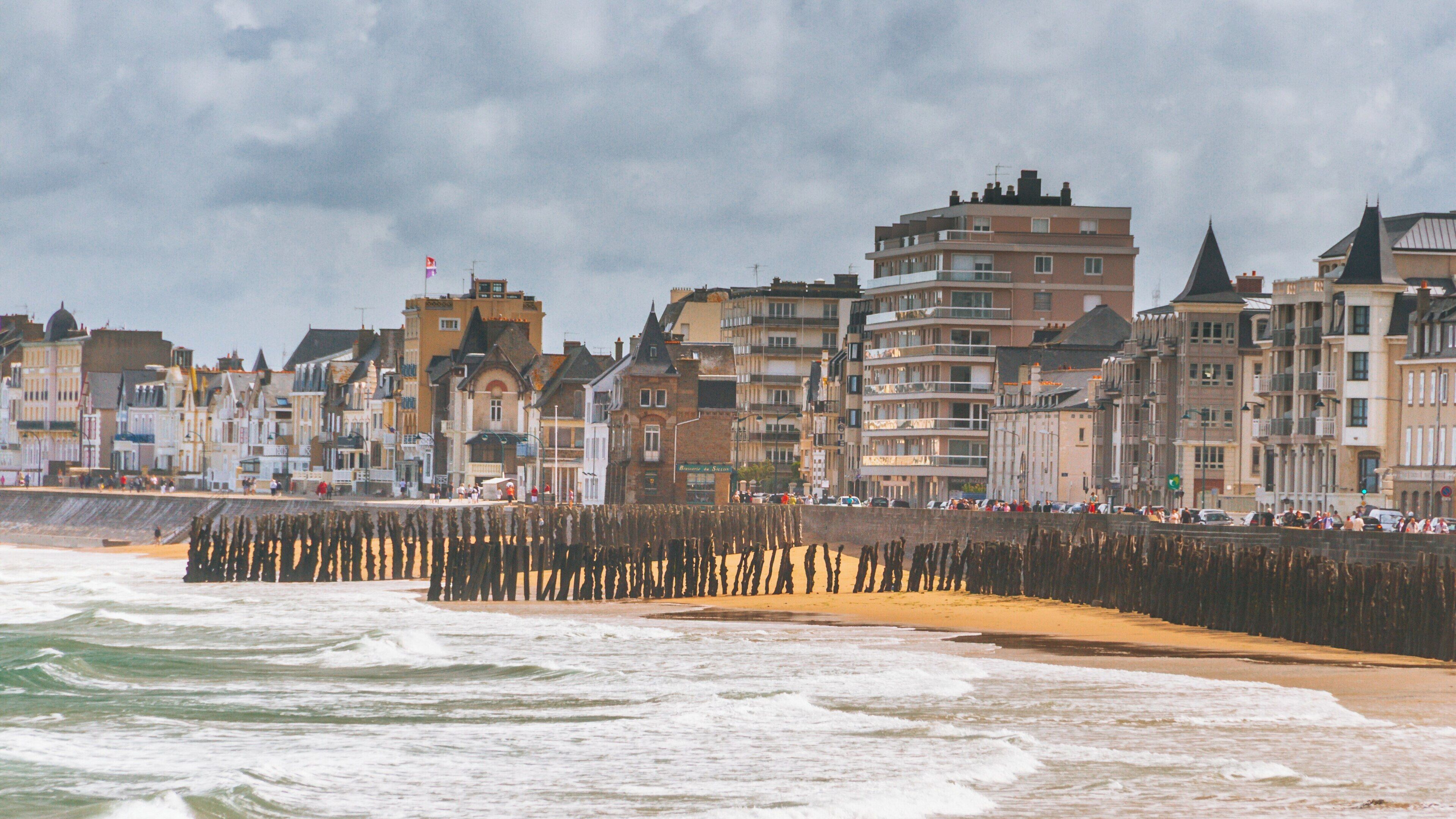 Grande Plage in Courtoisville-Sillon-Moka, Saint-Malo, offers a beautiful seaside view with charming buildings and dramatic waves under a moody sky
