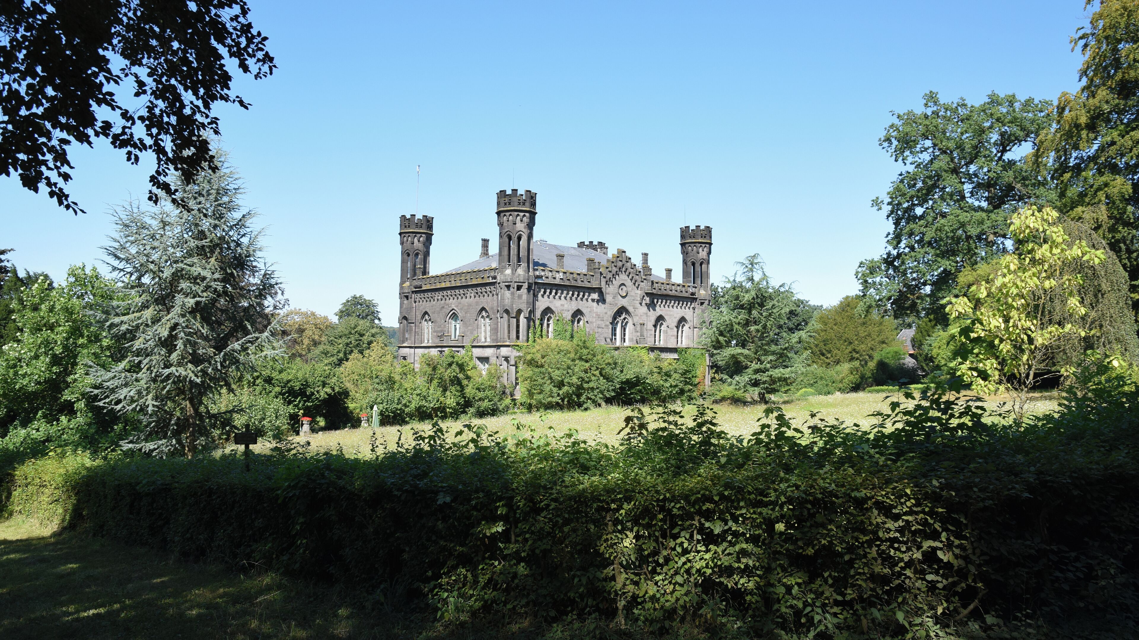 A large, historic building with multiple towers and a well-maintained garden in front.