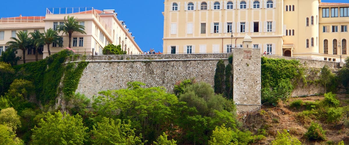 A coastal cityscape with historic buildings, a stone wall, and lush greenery.